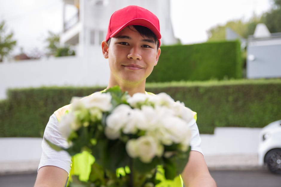 A cheerful flower delivery courier, wearing a bright red cap and a high-visibility yellow vest, smiling warmly as he presents a bouquet of fresh white flowers with green leaves, wrapped in clear plast