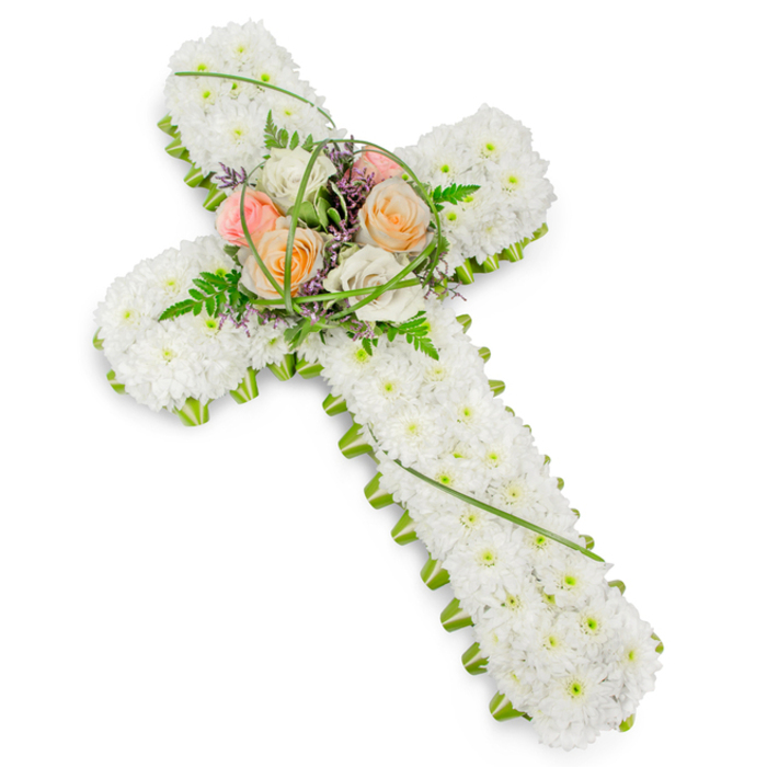 This image presents a solemn yet beautifully comforting floral cross, photographed against a clean white background so that every detail of the tribute stands out clearly. The cross itself is solid and three-dimensional, built with professional florist's care, then entirely covered with compact, pristine white chrysanthemums or similar small-headed blooms. Each flower head sits closely against its neighbour, creating a smooth, quilted texture that suggests serenity and spiritual purity, much like the quiet stillness you might feel stepping into a South Croydon church on a weekday afternoon. Along the edge of the cross, a crisp border of vivid green foliage and structural floral material traces the outline from top to bottom. This neat green edging not only supports the blooms but also provides a fresh, natural frame that highlights the strong Christian cross shape. At the centre, where the arms intersect, a raised spray of larger, more colourful flowers forms the emotional heart of the design. Roses in soft peach, gentle blush pink, and creamy white or ivory open in full, rounded blooms, their petals layered in delicate spirals. They are nestled among feathery green fern fronds, slim loops of bright bear grass, and tiny purple or lavender filler flowers that peep through, adding depth and a subtle play of colour. The lighting is bright but soft, with no harsh shadows, allowing the gentle hues and textures to be clearly seen. This floral cross would be at home on an easel beside the coffin at a South Croydon funeral service, or laid at a graveside in Queen's Gardens or a nearby cemetery, offering a heartfelt expression of faith, remembrance, and peaceful farewell.