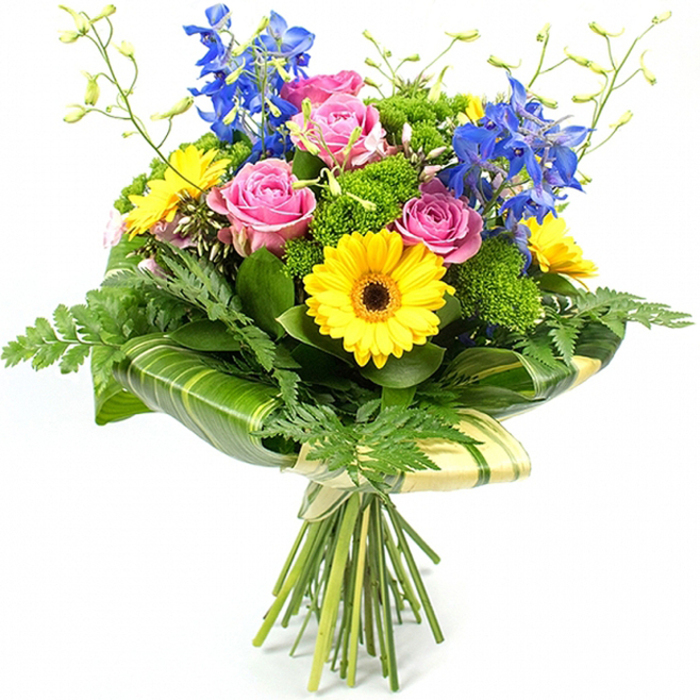 This hand-tied bouquet is captured upright against a bright white background, every detail clearly visible, as though the flowers have just been arranged on a workbench in a South Croydon shop. A cluster of fully opened pink roses forms the romantic focal point, their petals layered in soft, concentric whorls that create a plush, almost velour-like texture. Interspersed among them, bold yellow gerbera daisies flash their sunshine tones, each bloom displaying a distinctive dark brown centre that creates a strong contrast and makes the flowers appear even more vivid. Stretching upwards from behind, graceful stalks of deep blue delphinium blossoms introduce cool colour and height, their tiered florets evoking cottage garden borders and the calm of a clear sky after rain.   

A rich variety of greenery envelopes these statement blooms, rounding out the bouquet with a lush, abundant profile. Fine, delicate fern fronds spring from the sides and lower edges, adding feathery movement, while broad, glossy leaves in dark green hug the inner structure, ensuring the colourful flowers stand out crisply. Between the main stems, tufts of bright, textured filler foliage sit like tiny cushions of green, bringing depth and a lightly wild, garden-inspired feel. Around the lower portion of the flower heads, wide tropical-style leaves are wrapped snugly into a smooth collar, some marked with subtle lighter stripes that contribute an understated sophistication to the design.   

Below this leafy band, the natural stems are pulled tightly together and secured with a pale, fabric-like wrap, tied with a simple bow that underscores the handcrafted character of the arrangement. The overall impression is one of joyful elegance and modern charm, perfect as a centrepiece on a South Croydon dining table or a heartfelt gift for birthdays, anniversaries, or congratulations delivered across the local neighbourhoods.